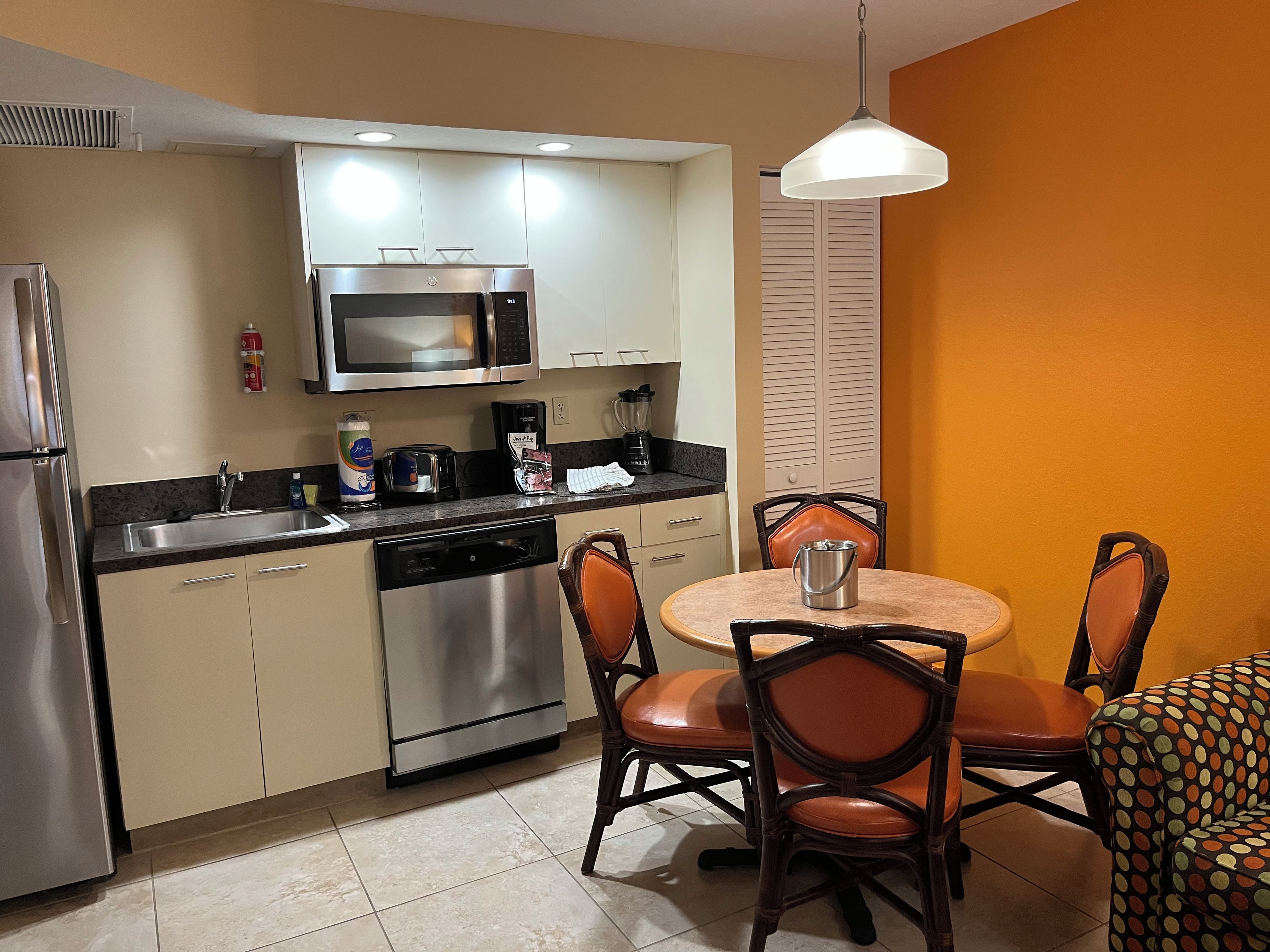 A compact kitchen with a microwave, toaster, and coffee maker, a dining table with chairs, and a dishwasher.