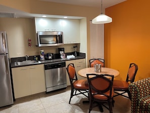 A compact kitchen with a microwave, toaster, and coffee maker, a dining table with chairs, and a dishwasher. - Vacation Village at Bonaventure (Weston)