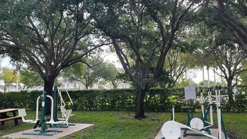 Outdoor exercise equipment in a park with trees and a bench.