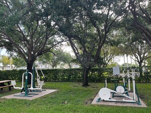 Outdoor exercise equipment in a park with trees and a bench. - Vacation Village at Bonaventure (Weston)
