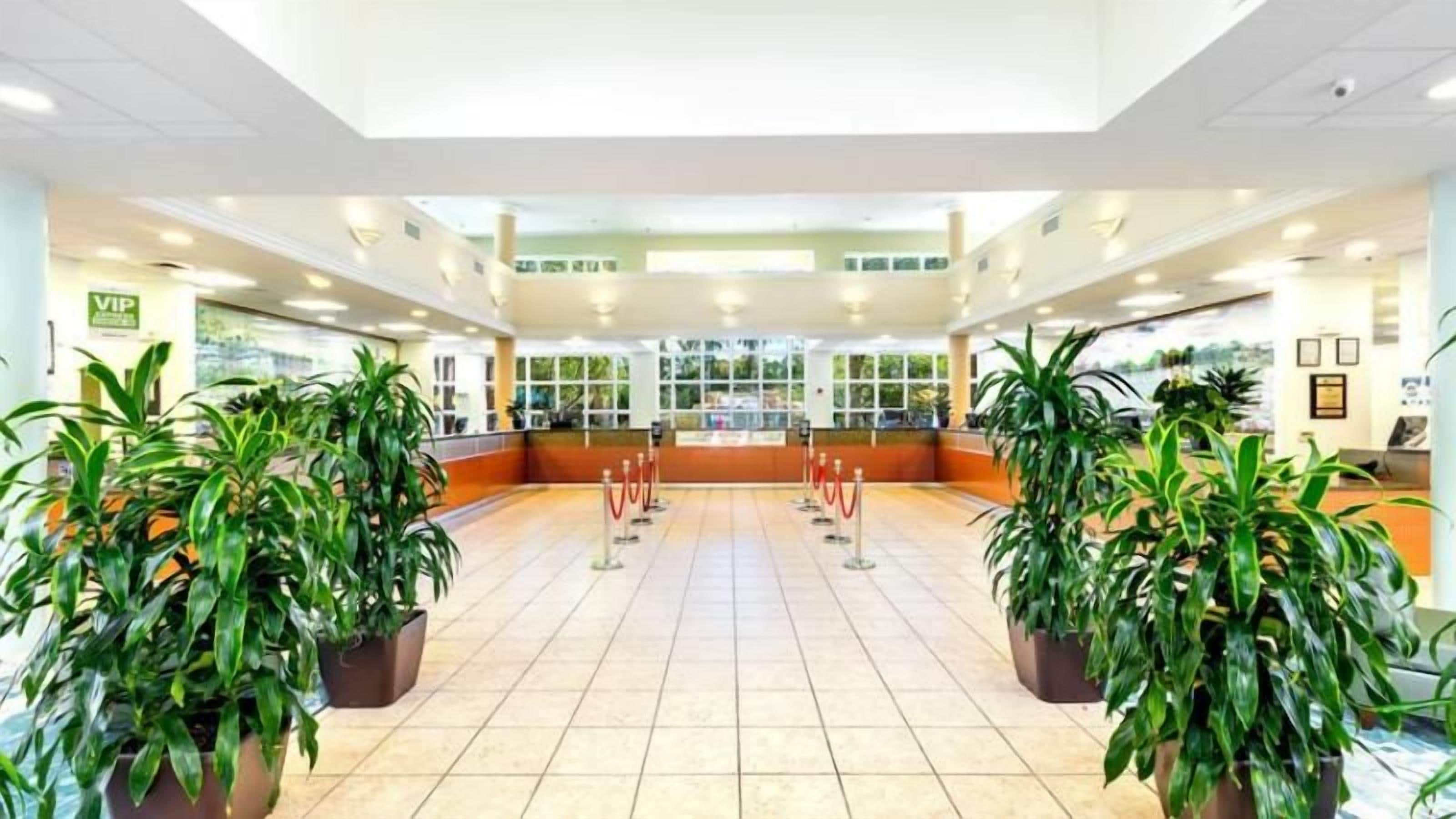 A spacious lobby with a tiled floor, potted plants, a reception desk, and a glass partition.