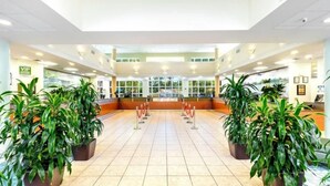 A spacious lobby with a tiled floor, potted plants, a reception desk, and a glass partition.