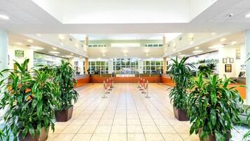 A spacious lobby with a tiled floor, potted plants, a reception desk, and a glass partition.