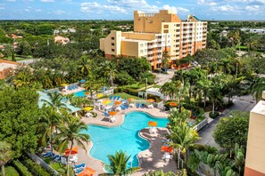 A hotel with a swimming pool, palm trees, and a large building in the background. - Vacation Village at Bonaventure (Weston)