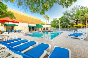 A pool area with lounge chairs and umbrellas, a building with a sign, and trees in the background. - Vacation Village at Bonaventure (Weston)