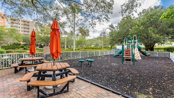 A park with picnic tables, playground equipment, and a fenced area.