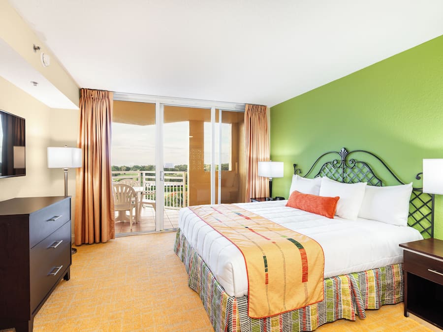 A hotel room with a large bed, a desk, a chair, and a balcony with curtains.