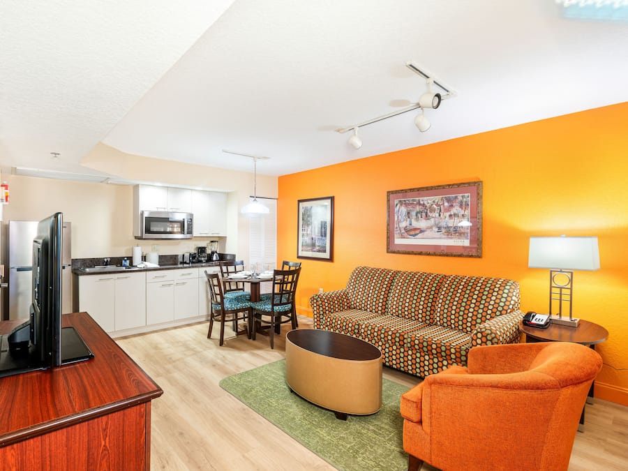 A compact living space with a kitchenette, a sofa, a dining table with chairs, and a television.