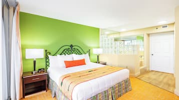 A hotel room with a green wall, a white bed with an orange pillow, two bedside tables with lamps, a mirror, and a door.