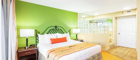 Habitación de hotel con pared verde, cama blanca con almohada naranja, dos mesitas de noche con lámparas, un espejo y una puerta.