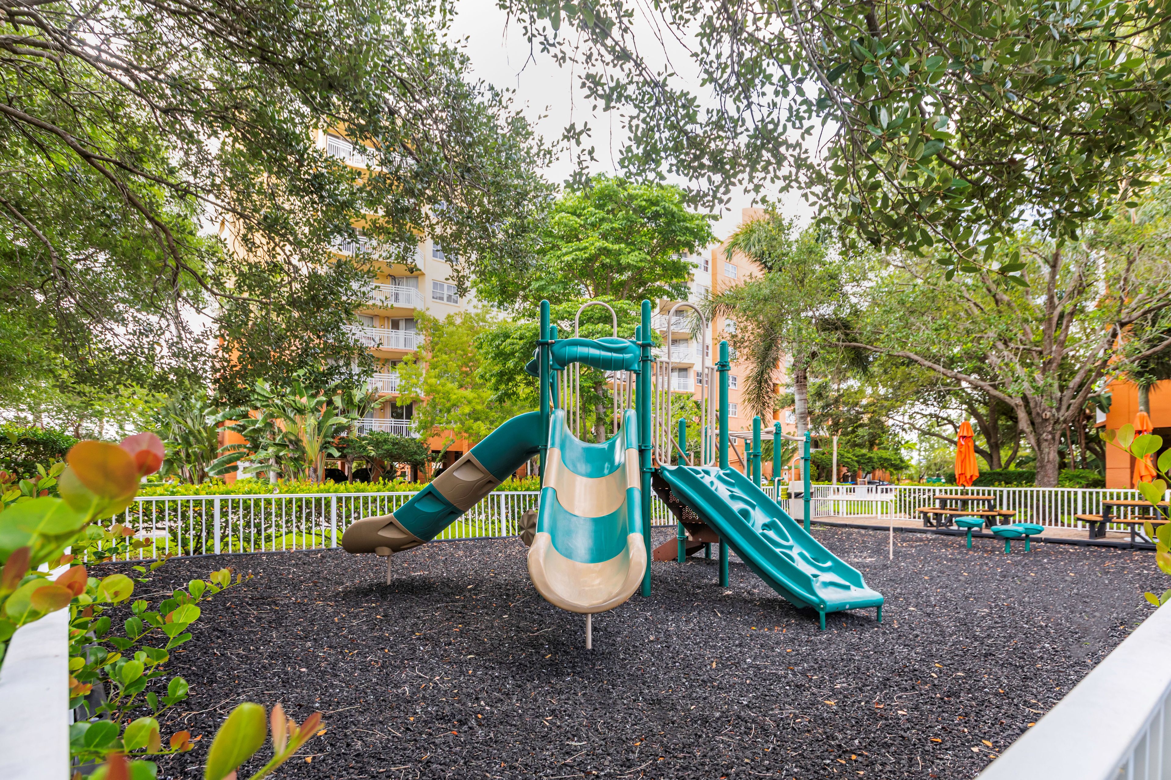 A playground with slides and climbing structures, surrounded by trees and a fence.