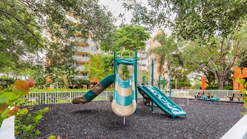A playground with slides and climbing structures, surrounded by trees and a fence.