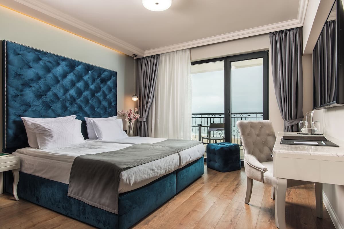 A modern hotel room with a large bed, a desk, and a balcony with curtains.