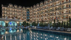 Un hotel de varios pisos con zona de piscina, con balcones que tienen jardineras y mobiliario de exterior.
