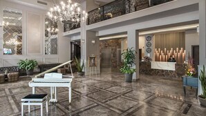 Un lobby espacioso con un piano de cola, una araña de cristal y una recepción.