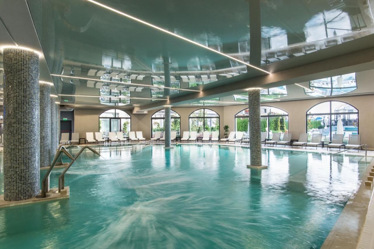 An indoor swimming pool with clear water, surrounded by lounge chairs and large windows.