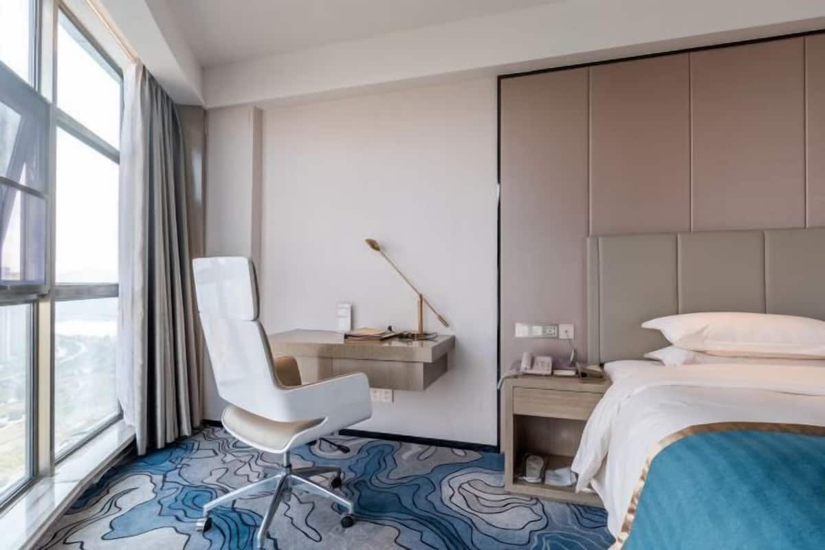 Habitació d'hotel amb un llit, una taula de treball amb una cadira, una finestra i vistes a la ciutat.