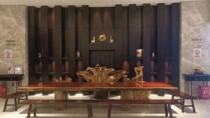 Een grote houten eettafel met banken in een kamer met donker houten paneelwerk en een decoratief kunstwerk erboven.