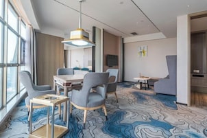 Quarto de hotel moderno com área de refeições, janelas amplas e carpete estampado.