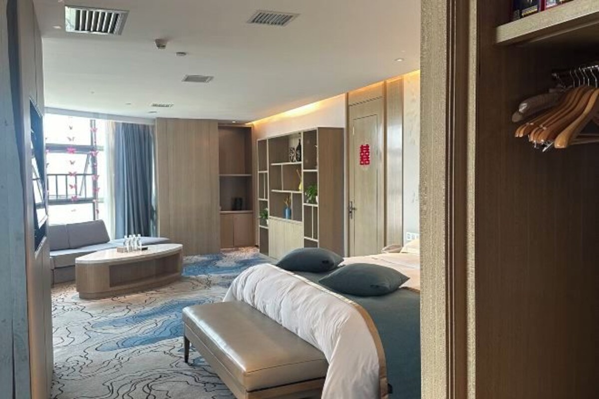 Habitación de hotel con cama, un banco, una zona de estar con mesa y un armario con ropa colgada.