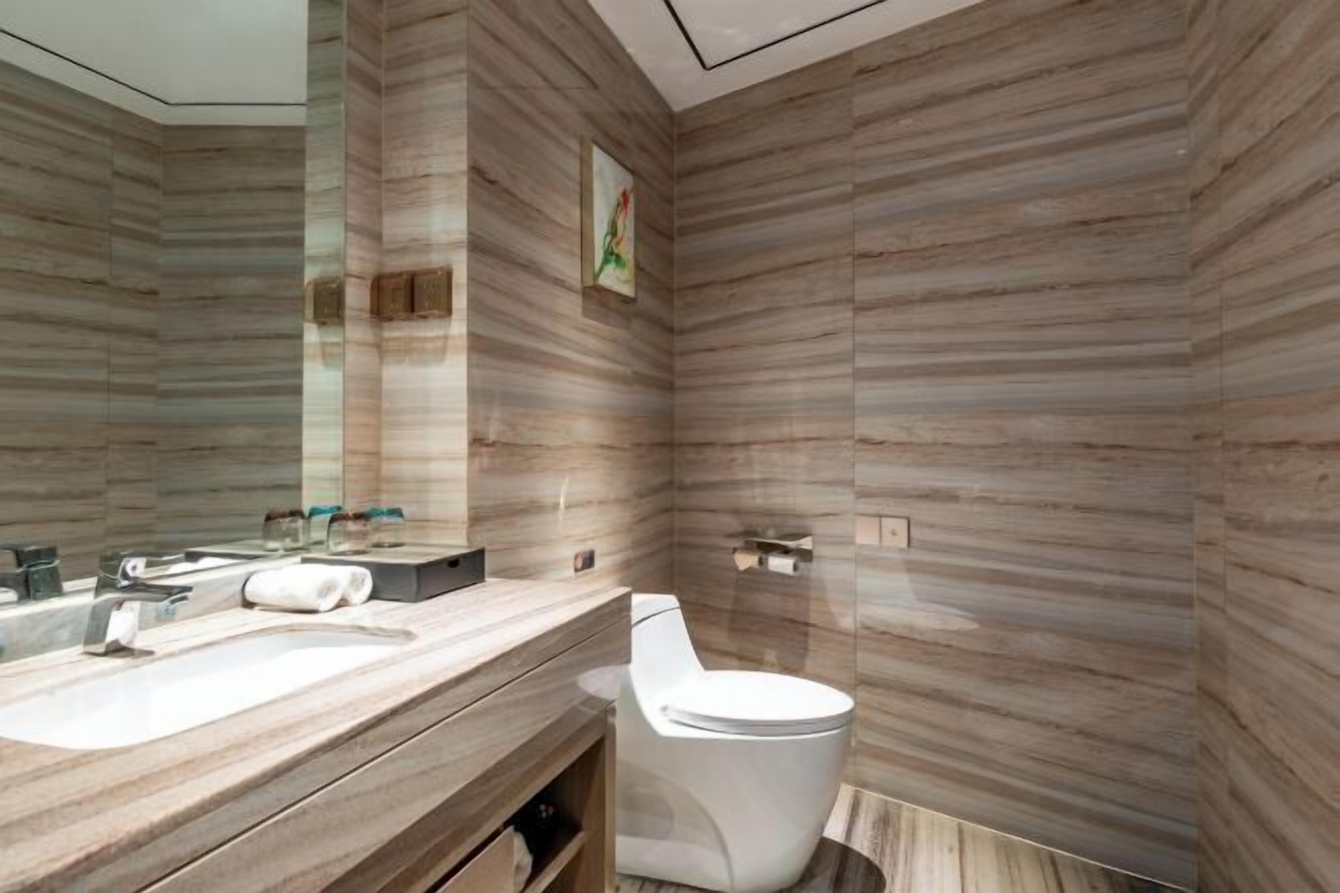 Un baño moderno con diseño de pared de madera, un espejo grande, un inodoro y un mueble de tocador con lavamanos y toalla.