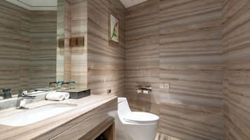 Un baño moderno con diseño de pared de madera, un espejo grande, un inodoro y un mueble de tocador con lavamanos y toalla.