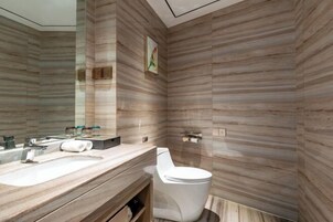A modern bathroom with a wooden wall design, a large mirror, a toilet, and a vanity with a sink and towel.