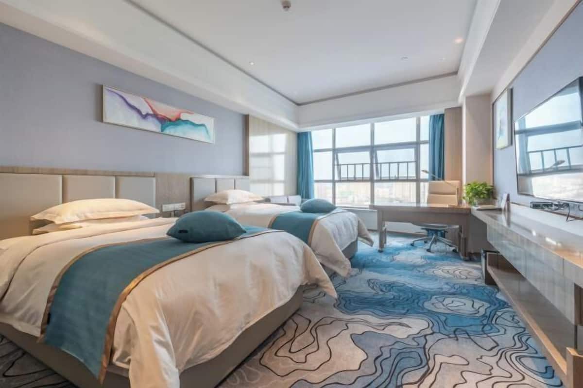 Habitació d'hotel amb dos llits, una taula de treball i un gran finestral.