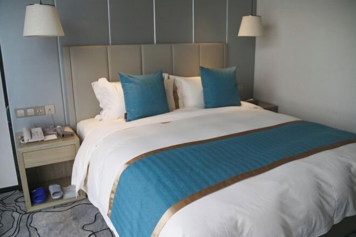 Habitación de hotel con cama, mesitas de noche, lámpara y suelo alfombrado.