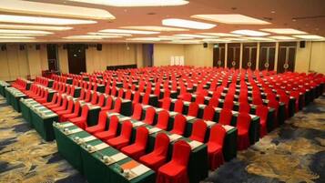 Une salle de conférence avec des rangées de chaises et de tables, un sol recouvert de moquette et un plafond doté d’un éclairage encastré.
