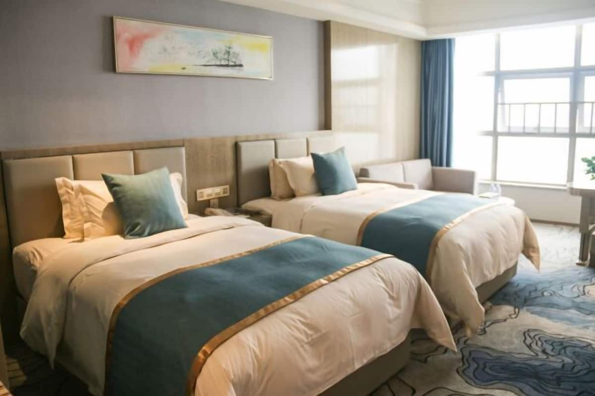 Habitació d'hotel amb dos llits, una nit, una cadira i una finestra amb cortines.