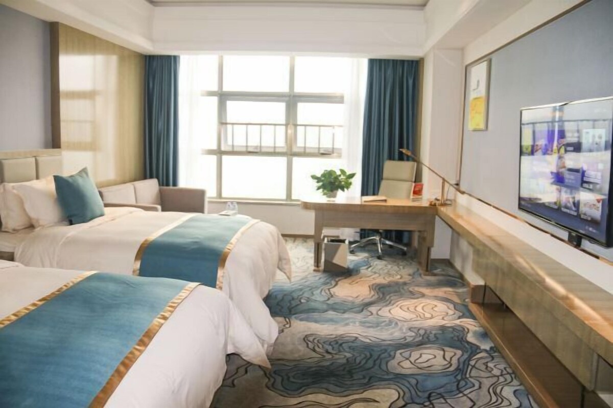 Habitación de hotel con dos camas, un escritorio, televisor y una ventana grande con cortinas.