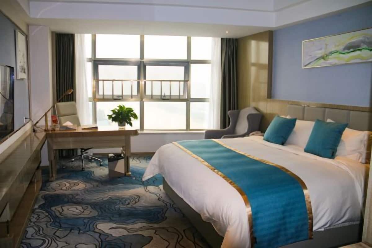 Habitació d'hotel amb un llit gran, un escriptori amb cadira, una televisió i una finestra amb cortines.
