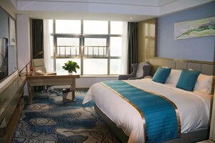 Habitación de hotel con una cama grande, un escritorio con silla, un televisor y una ventana con cortinas.