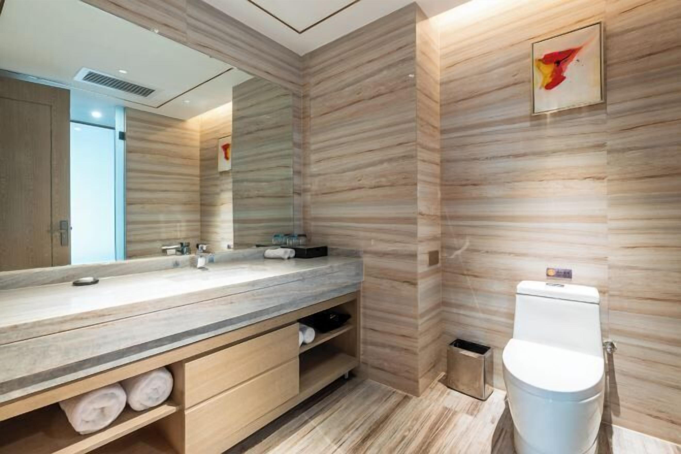 Un baño moderno con un mueble de tocador de madera, un espejo grande y un inodoro.