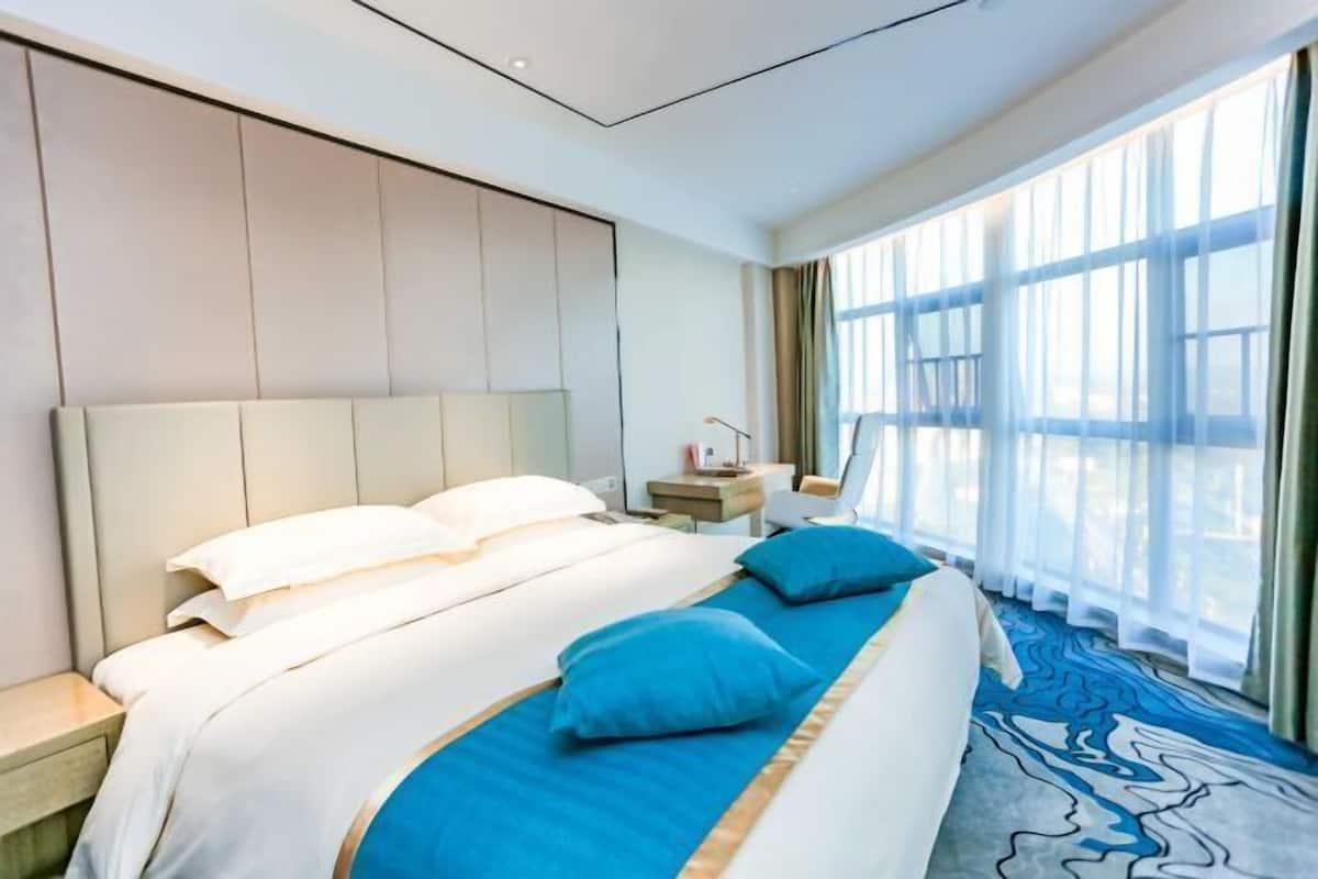 Habitació d'hotel amb un llit gran, una taula de nit, un escriptori i vistes a l'exterior a través de grans finestres.