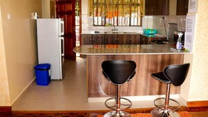 A kitchen with a central island, two bar stools, a refrigerator, and wooden cabinets.