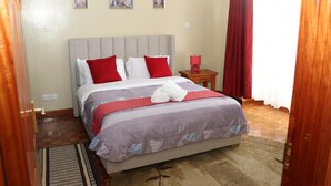 A neatly arranged bedroom with a bed, a nightstand, a wall-mounted lamp, and a window with curtains.