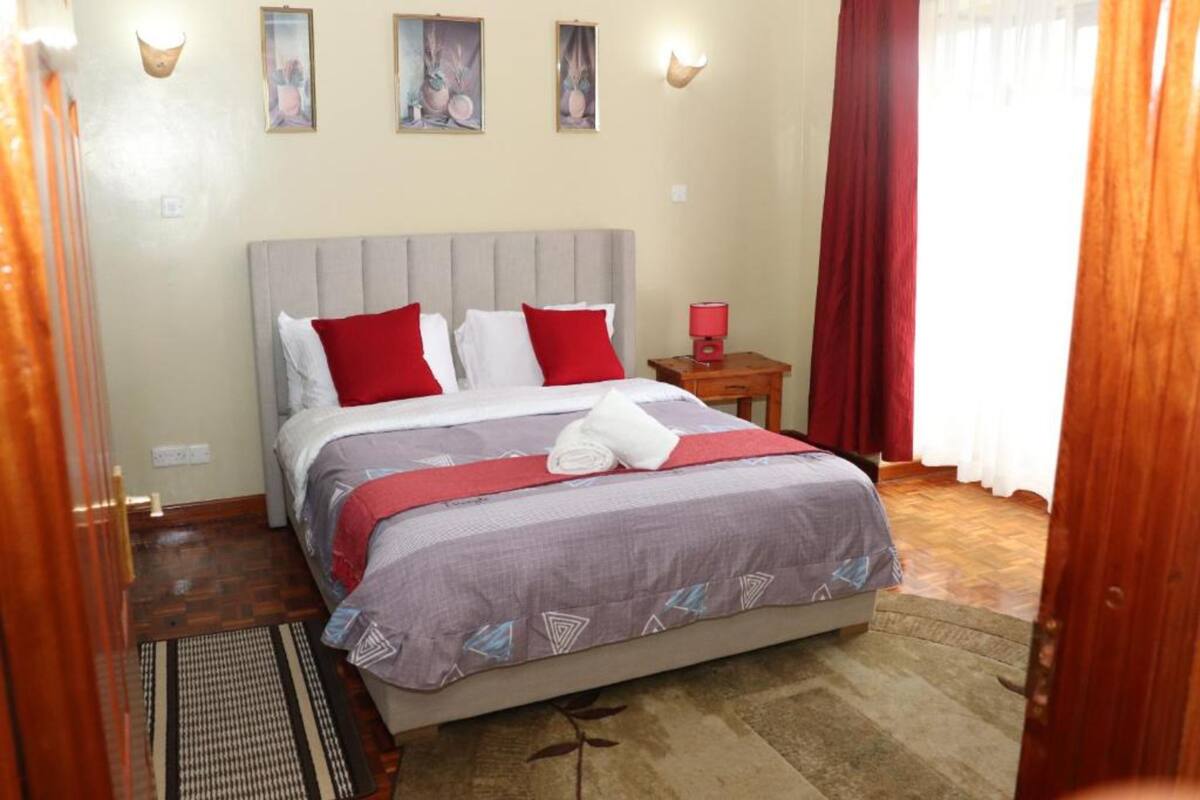 A neatly arranged bedroom with a bed, a nightstand, a wall-mounted lamp, and a window with curtains.