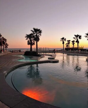 A pool area with palm trees and lounge chairs, surrounded by a low wall. - Crystal Tower, 3 pools, 2 hot tubs 2 bed 2 bath great amenities, great location (Gulf Shores)