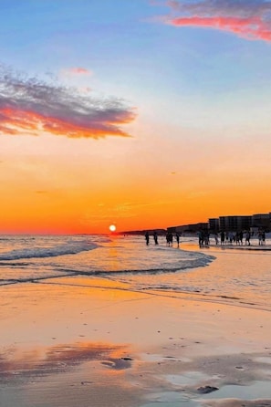 Eine Strandansicht mit Sonnenuntergang, Wellen und Menschen am Ufer.