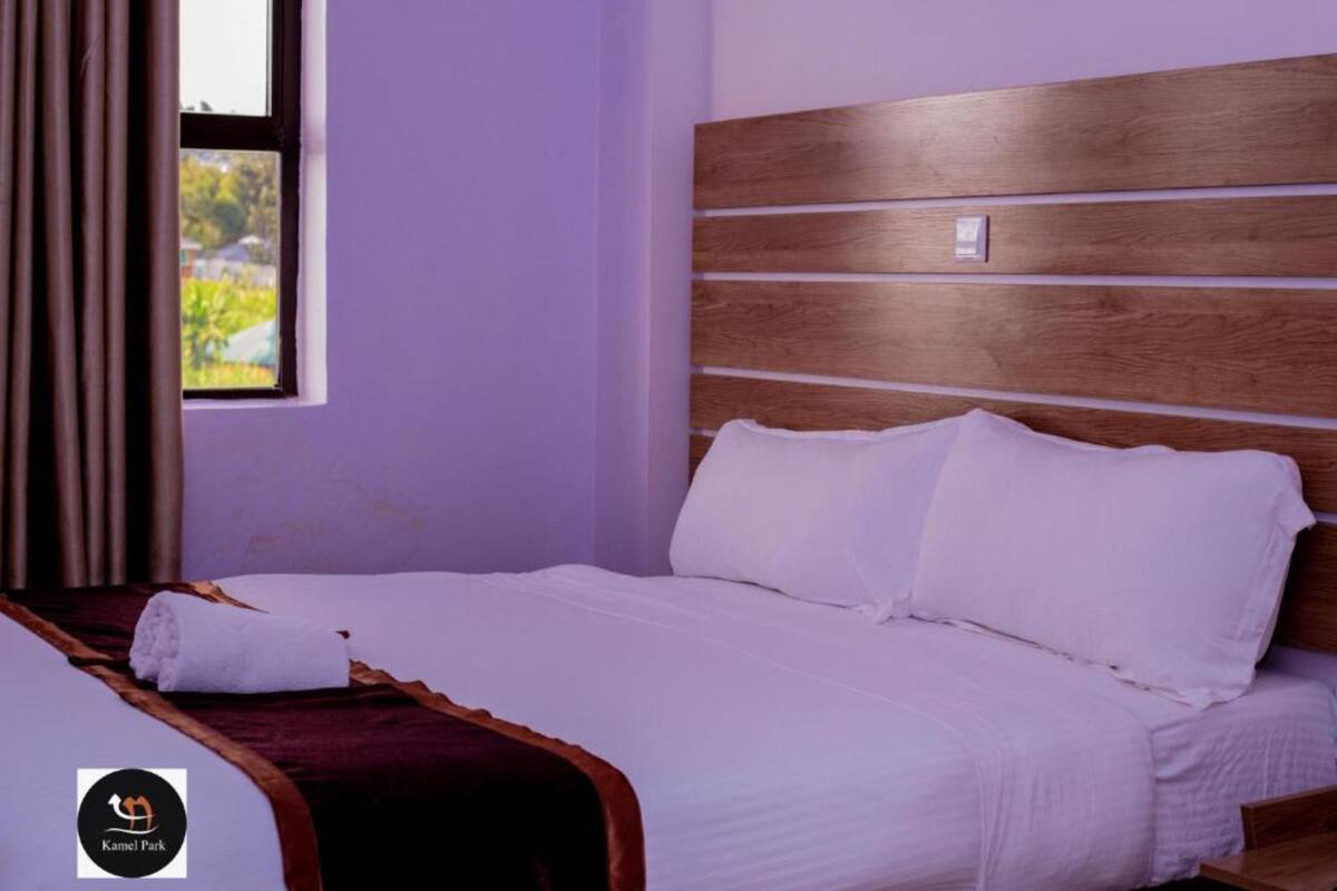A neatly made bed with white linens and a wooden headboard in a room with purple walls.