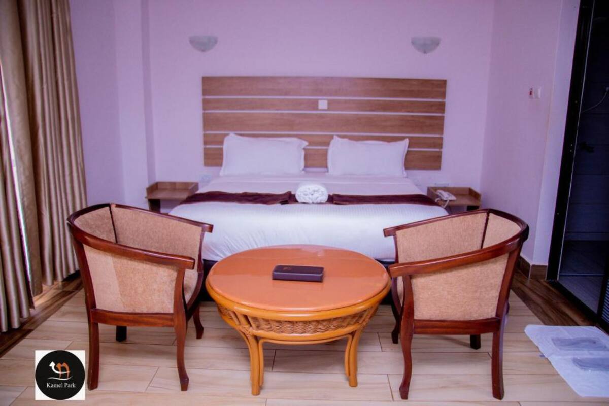 A hotel room with a bed, two armchairs, a small round table, and a nightstand with a lamp.