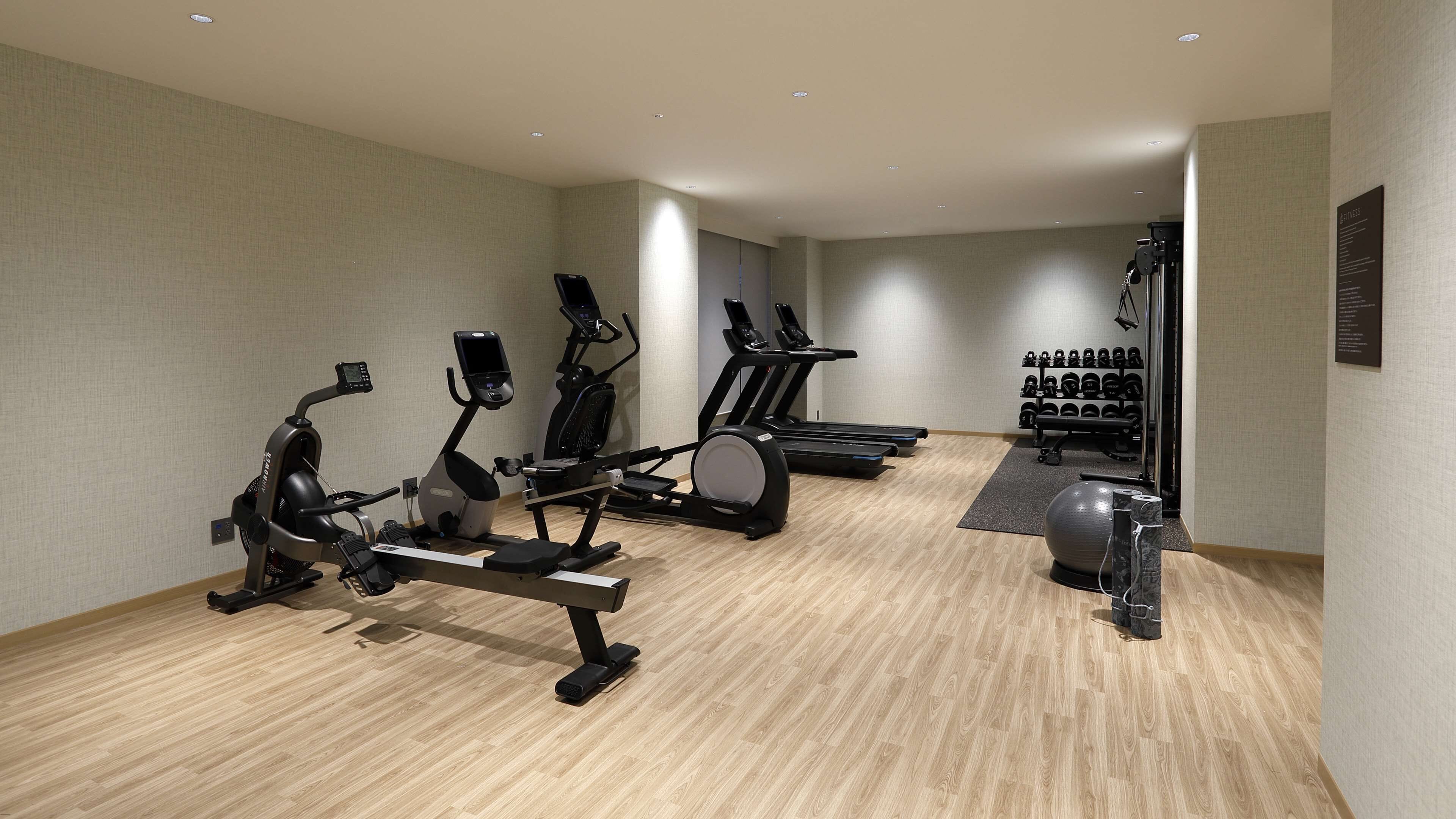A gym with cardio machines, a rowing machine, a treadmill, and a set of dumbbells.