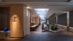 Un moderno vestíbulo de hotel con un mostrador de recepción alargado, señalización direccional y una escalera que lleva a los pisos superiores.