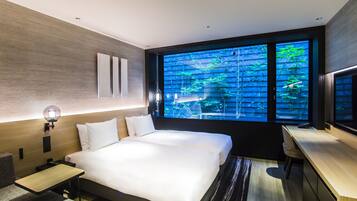 A modern hotel room with a large bed, bedside tables, a desk, and a large window with a view of greenery.