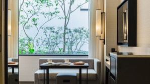 Una habitación moderna con sofá, una mesita con dos tazas y un libro, televisión y ventana con vistas a árboles.