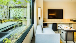 Habitación de hotel moderna con un ventanal grande, un televisor de pantalla plana, un sofá, una mesita pequeña y una kitchenette.