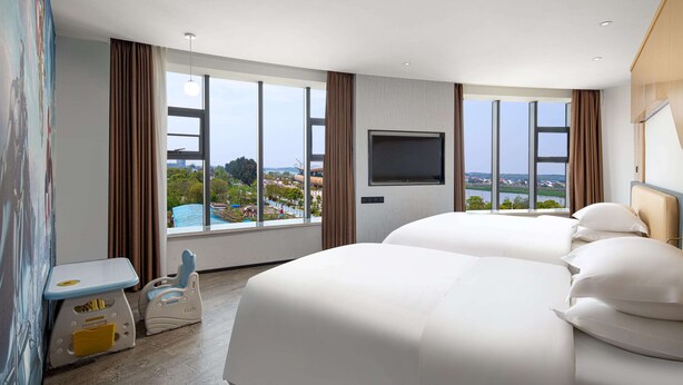 A hotel room with two beds, a TV, and a large window offering a view of a cityscape. - Microtel by Wyndham Miluo Downtown Hotel (Yueyang)