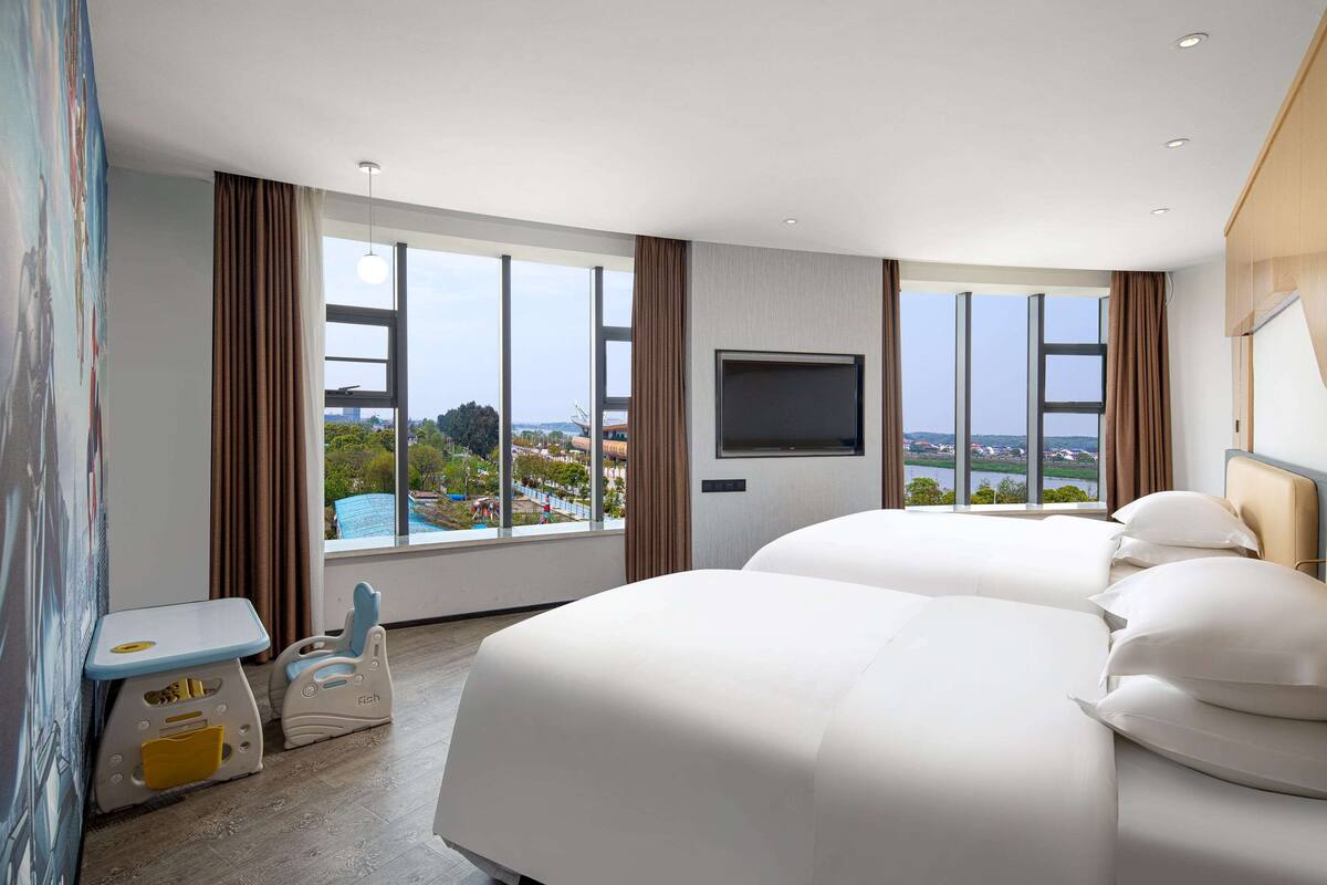 Une chambre d’hôtel avec deux lits, une télévision et une grande fenêtre donnant sur un paysage urbain.